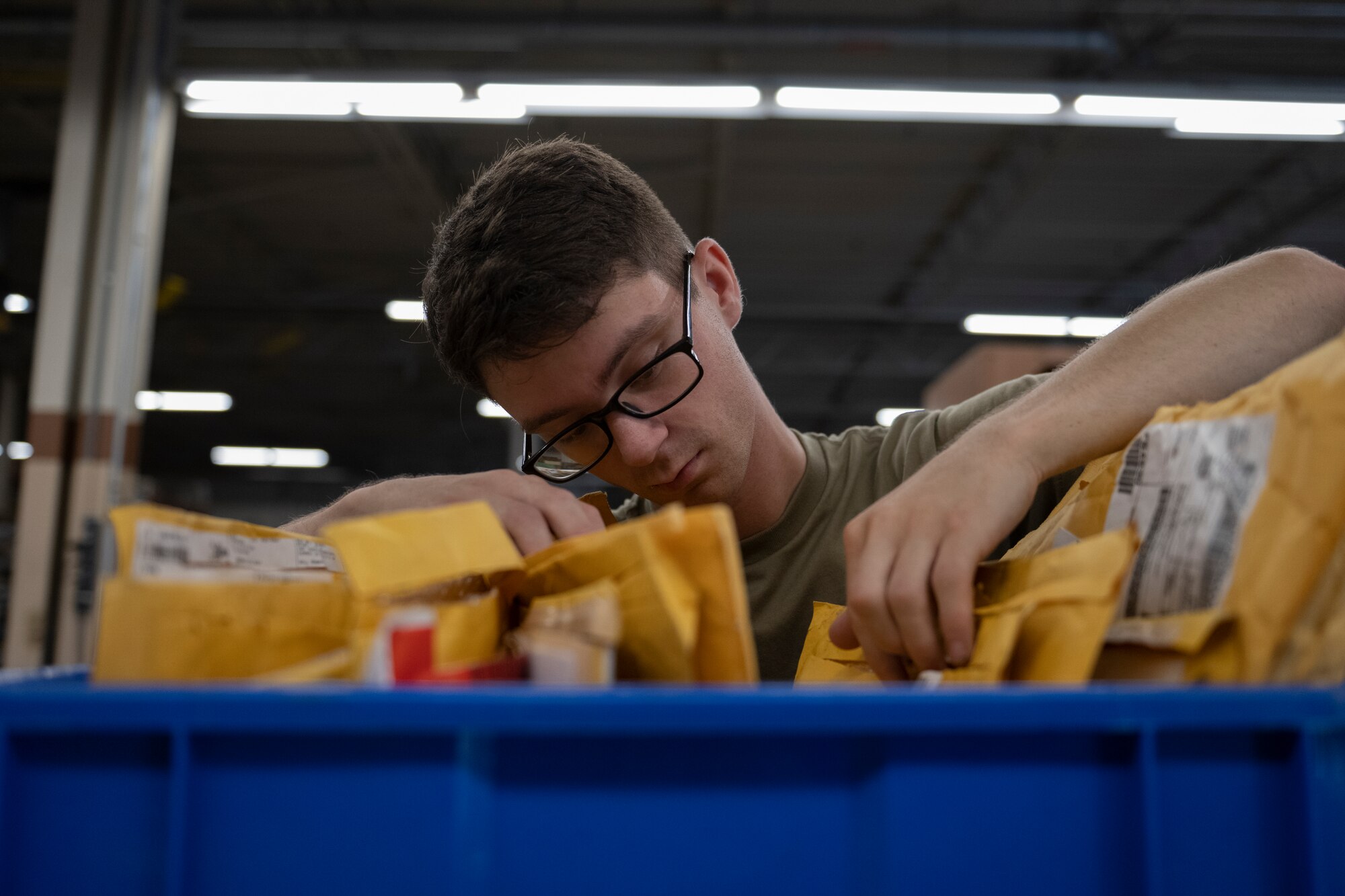 A photo of a blue box with several orange manilla envelopes, and there is a person sorting through them.