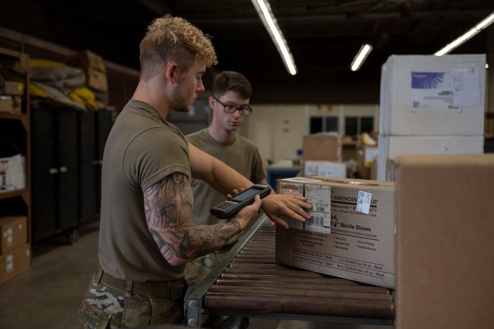 A photo of two people standing in a warehouse with boxes in front of them, scanning a box.
