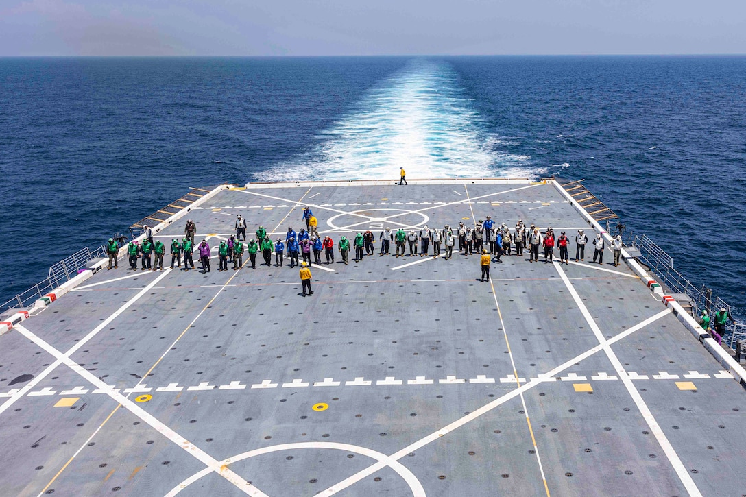 Marines and sailors stand in a line on the deck of a ship.