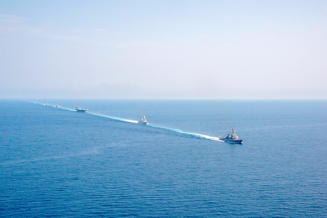 Ships sail in formation in body of water.