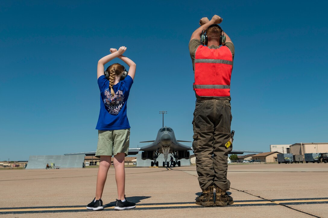 An airman and military child cross their hands above their heads in front of an aircraft.