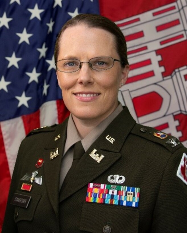 Graphic illustration of a woman wearing the Class A uniform of the US Army, with the rank of colonel. She is wearing glasses.