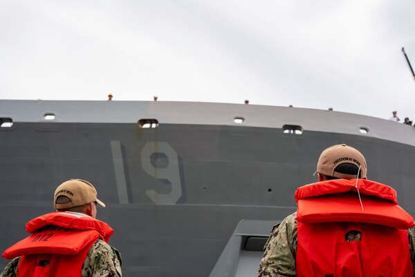 Aviation Boatswain’s Mate (Aircraft Handling) Airman Khen Muang, left, and Seaman Jesse Gross, assigned to the aircraft carrier USS George H.W. Bush (CVN 77), watch as the amphibious transport dock USS Mesa Verde (LPD 19) pulls away from the pier, departing Naval Station Norfolk for a scheduled deployment, July 10, 2023.