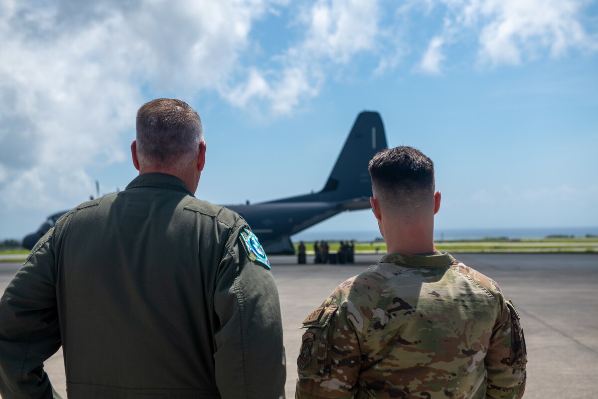 Airmen looking across the flight line to a jet getting unloaded.