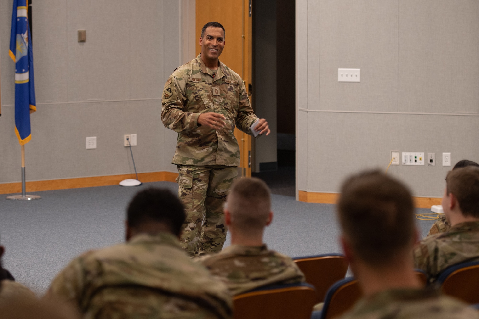 An enlisted chief stands in front of the room, smiling at attendees.
