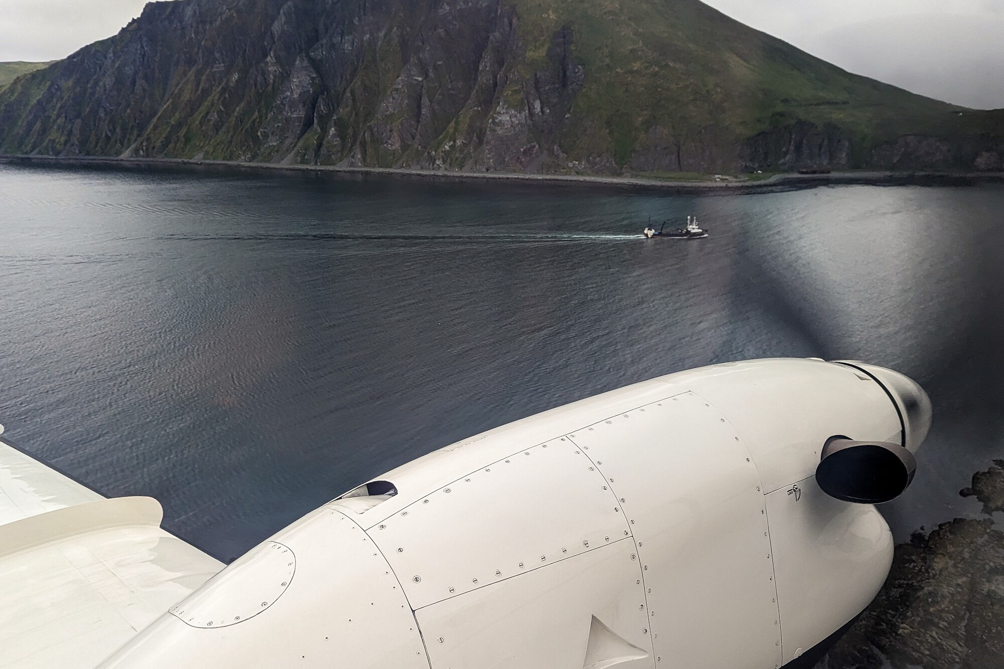 A photo of a C-12J Huron flying past a rocky island cliff.