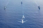 A U.S. Navy P-8 Poseidon flies above a formation of surface ships and submarines from the United States, Japan, and the Republic of Korea in the Philippine Sea during Pacific Vanguard 23