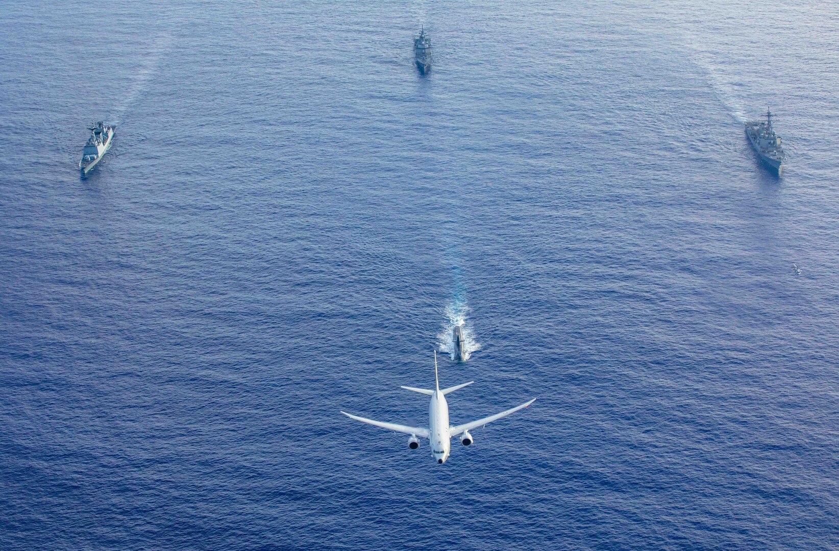 A U.S. Navy P-8 Poseidon flies above a formation of surface ships and submarines from the United States, Japan, and the Republic of Korea in the Philippine Sea during Pacific Vanguard 23