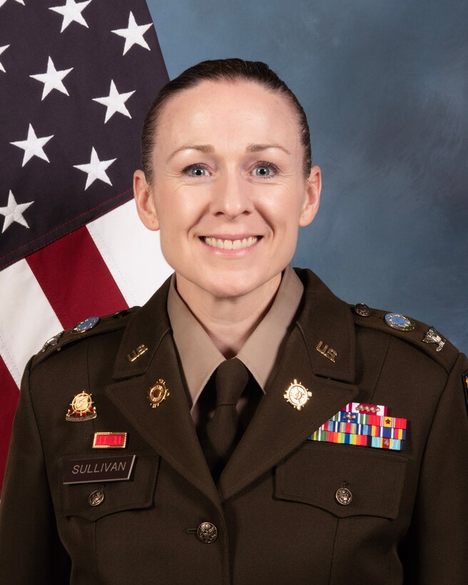 A portrait of COL Adrian Sullivan in Army dress uniform in front of an American flag
