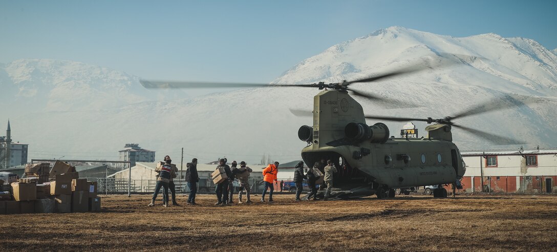 U.S. Army soldiers assigned to 3rd Battalion, 501st Aviation Regiment, Combat Aviation Brigade, 1st Armored Division (1AD CAB), and Turkish civilians offload humanitarian aid from a U.S. Army CH-47 Chinook helicopter in Elbistan, Türkiye, Feb. 18, 2023.