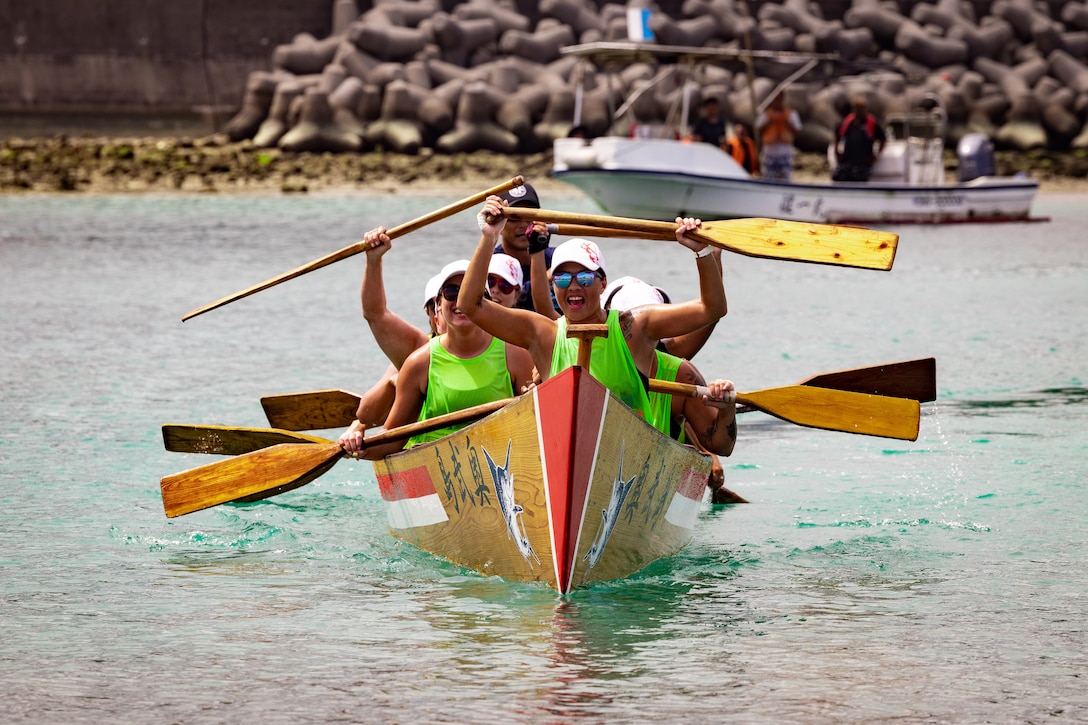 A group of people in a dragon boat smile and hold up their paddles.