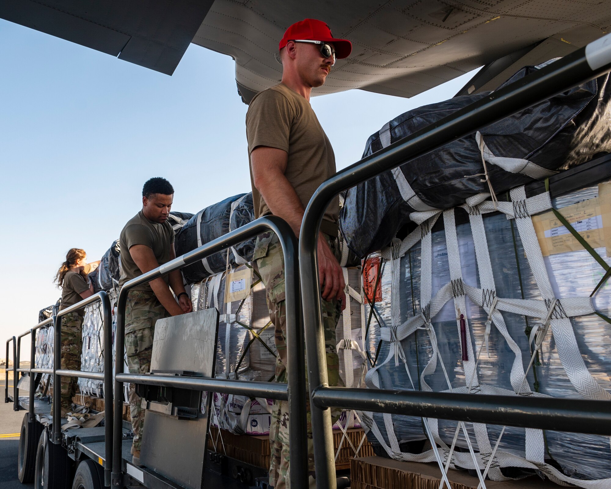 From right, U.S. Army Staff Sgt. Carson Brown, 165th Quartermaster Company parachute rigger, U.S. Army Specialist Bradan Duckworth, 165th QM Co. parachute rigger, and U.S. Air Force Senior Airman Desirae Holland, 40th Expeditionary Airlift Squadron C-130 loadmaster, stand ready to load container delivery systems (CDS) bundles onto an aircraft, at Ali Al Salem Air Base, Kuwait, July 5, 2023.