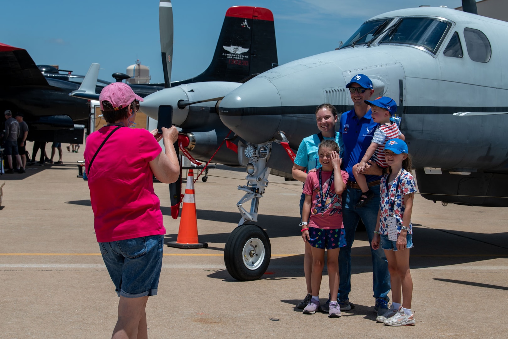 A family poses in front of a static display of a 137th Special Operations Wing MC-12W aircraft at the Tinker Air Show on July 1, 2023, at Tinker Air Force Base, Oklahoma City. The 137th SOW joined members of the total force at the Tinker Air Show, which showcased the diverse aspects of aviation. (U.S. Air National Guard photo by Airman 1st Class Erika Chapa)