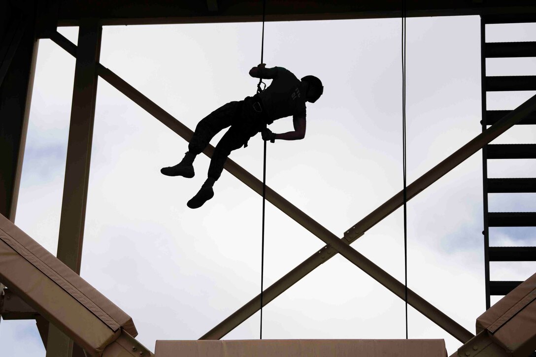 A Marine shown in silhouette rappels down a tower.