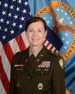 A portrait of Army Col. Faith Chamberlain in dress uniform with the American and Defense Logistics Agency flags behind her