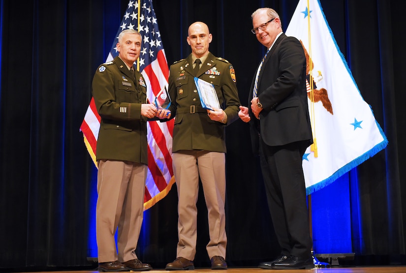 Three men stand near each other on a stage.