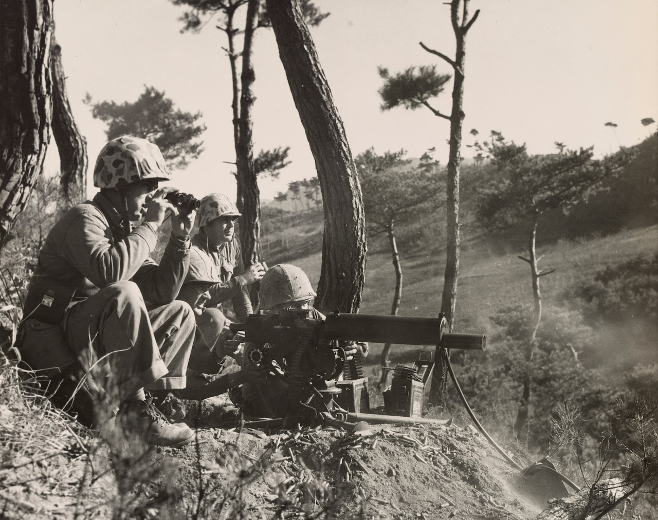 Four men look into the distance; one looks through the sight of a machine gun.