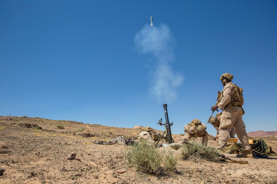 Three Marines take cover in a dirt field after firing a weapon into the air as a fellow Marine watches.