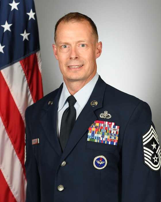 Chief Master Sgt. Christopher Griste, 20th Fighter Wing Command Chief bio photo in front of US flag on grey background