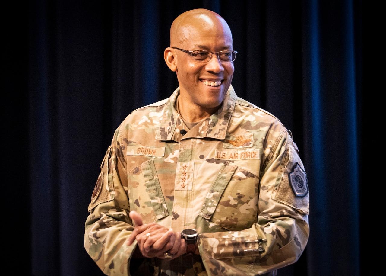 A man in military uniform, looking to his left, smiles.