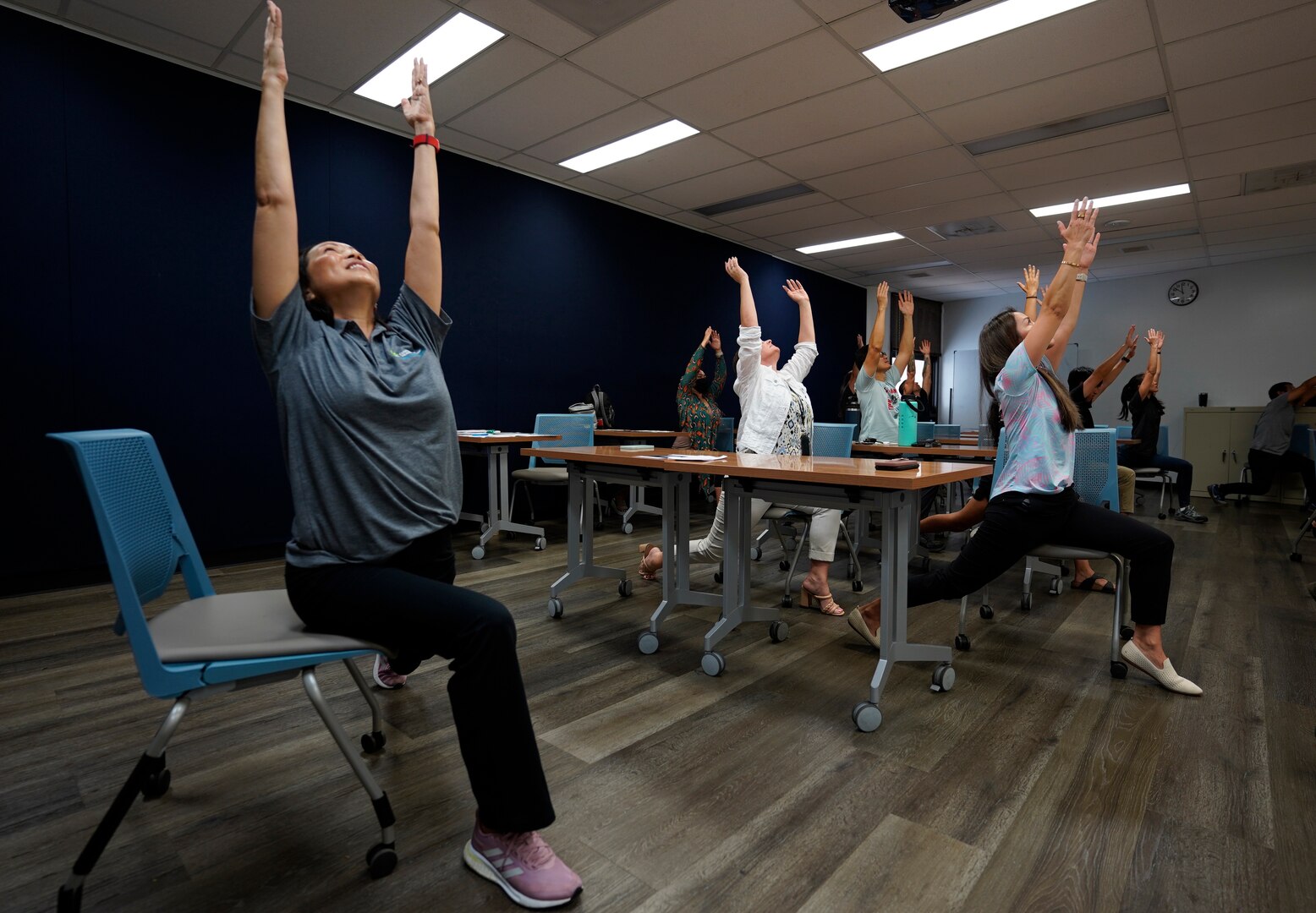 Mae Lynne from Kaiser Permanete, left, leads shipyard personnel through a yoga flow during a chair yoga stretch class at Pearl Harbor Naval Shipyard.