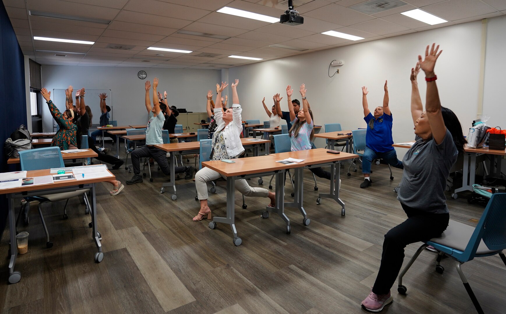 Mae Lynne from Kaiser Permanete, right, leads shipyard personnel through a yoga flow during a chair yoga stretch class at Pearl Harbor Naval Shipyard.