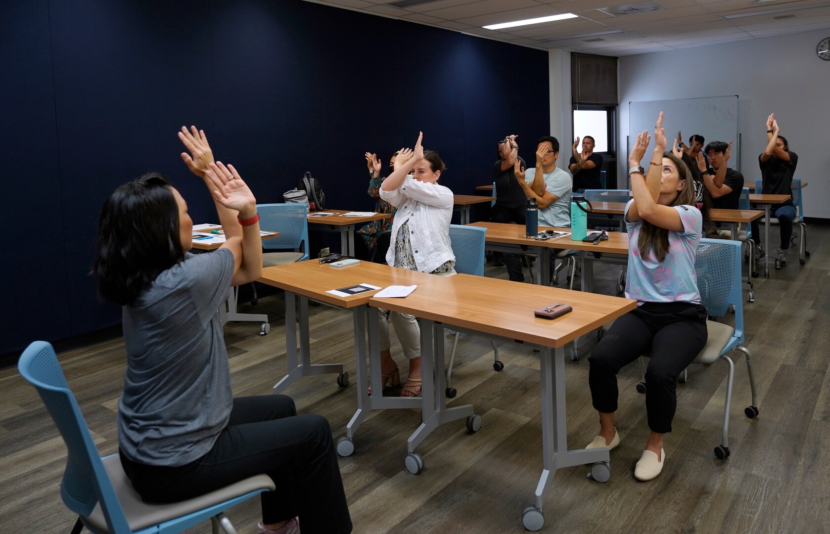 Mae Lynne from Kaiser Permanete, left, demonstrates a seated eagle pose as shipyard personnel mirror the pose during a chair yoga stretch class at Pearl Harbor Naval Shipyard.