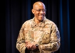 A man in military uniform, looking to his left, smiles.