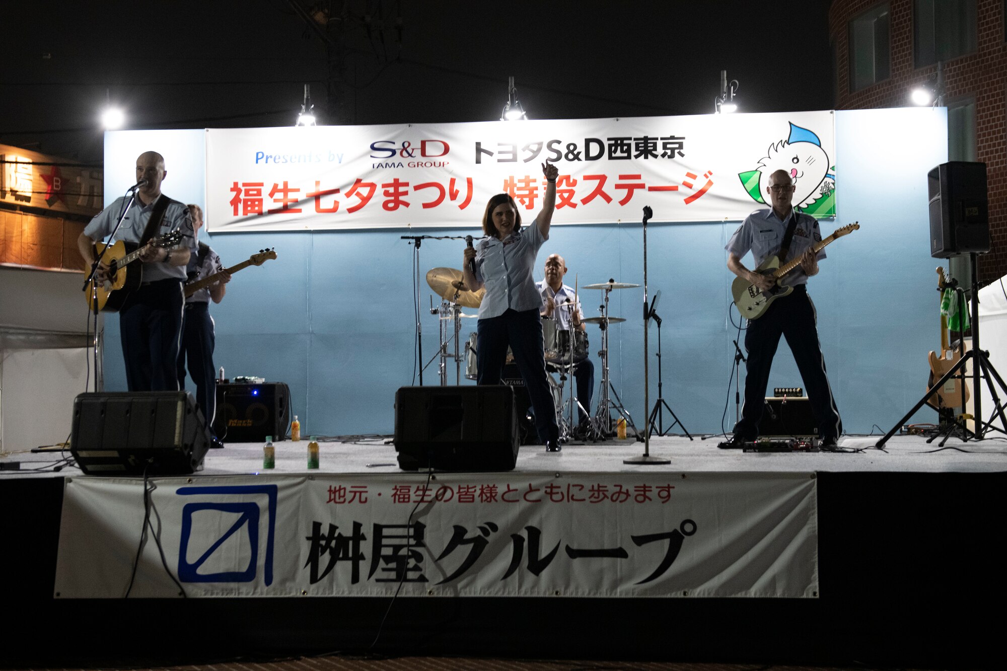A four member military band on a stage waving to a crowd