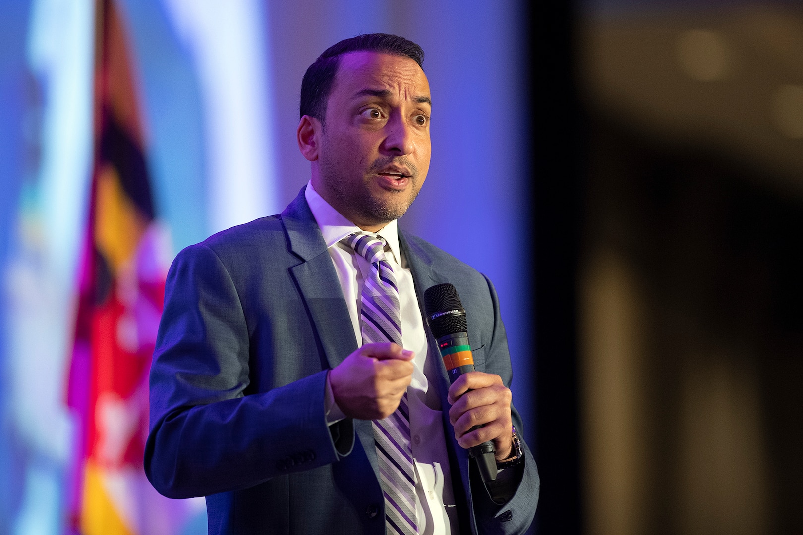 A man wearing business attire speaks while holding a microphone.