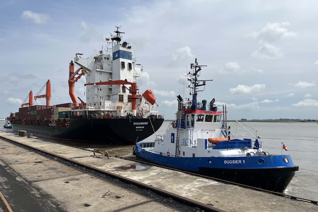 A container ship and tugboat sit dock side.