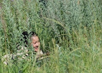 Tech. Sgt. Shareen Mendiola, 219th Security Forces Squadron defender, hides in vegetation in Mountrail County, North Dakota, July 7, 2023. Mendiola acted as a member of an opposing force during a security forces readiness exercise. (U.S. Air Force photo by Airman 1st Class Kyle Wilson)