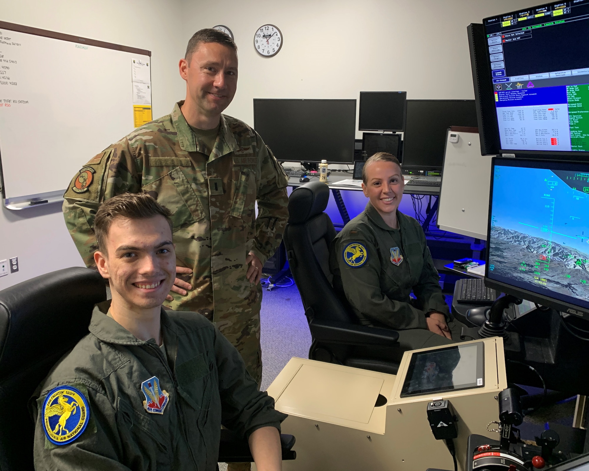 Two men and a woman, all in uniform, pose for a photo near an MQ-9 Flight simulator.