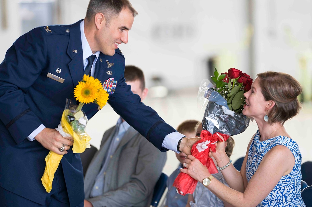 An airman hands flowers to a woman sitting in a crowd.