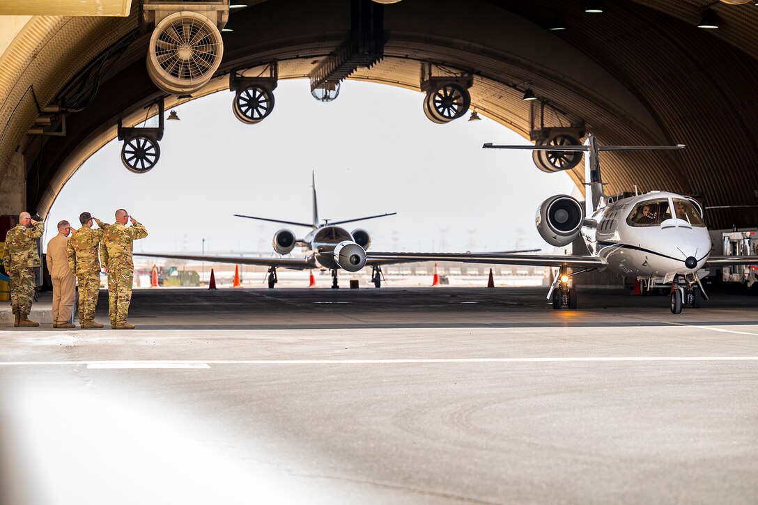 Airmen salute a military aircraft as it taxis on a runway.