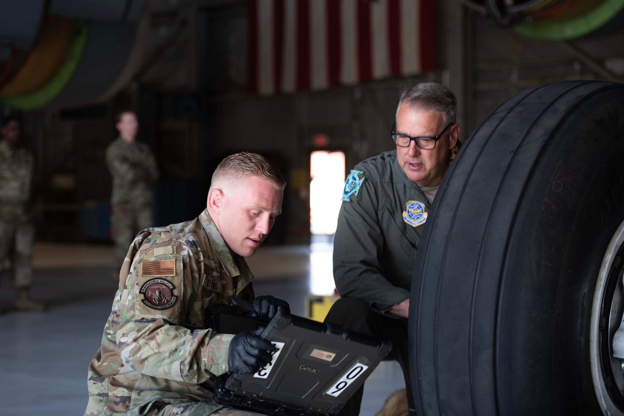 An Airman shows another Airman a computer behind a large tire.