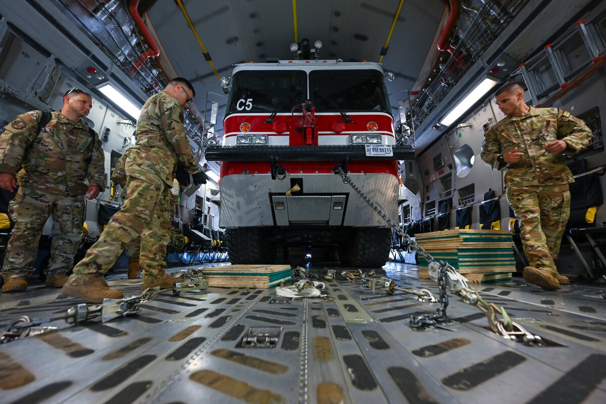 Photo of three individuals in the back of a C-17 in front of the firetruck.