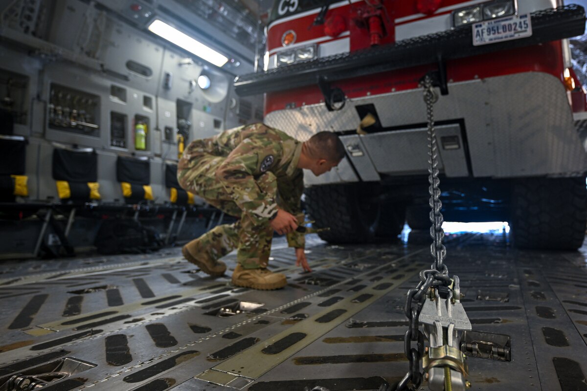 Photo of individual looking under a firetruck that's loaded onto a C-17.