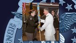 A Navy officer hands an Army officer a flag.