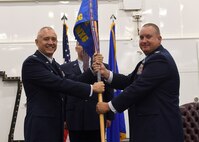 Two Air Force colonels wearing full dress uniforms pose with a blue flag with gold letters.