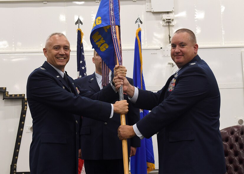 Two Air Force colonels wearing full dress uniforms pose with a blue flag with gold letters.