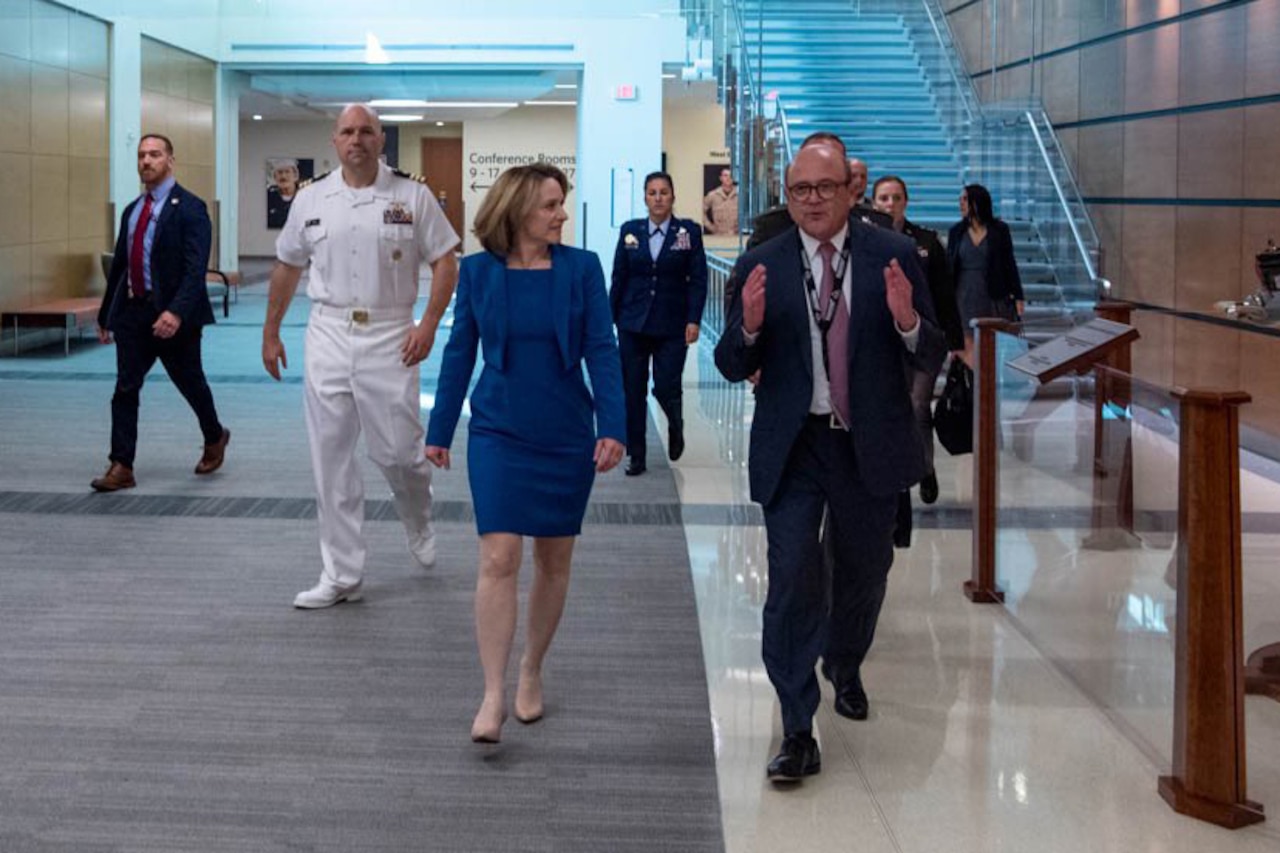 Deputy Defense Secretary Kathleen H. Hicks walks with a civilian in a lobby-type room.