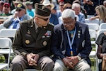 Two men sit next to each other outdoors and talk.