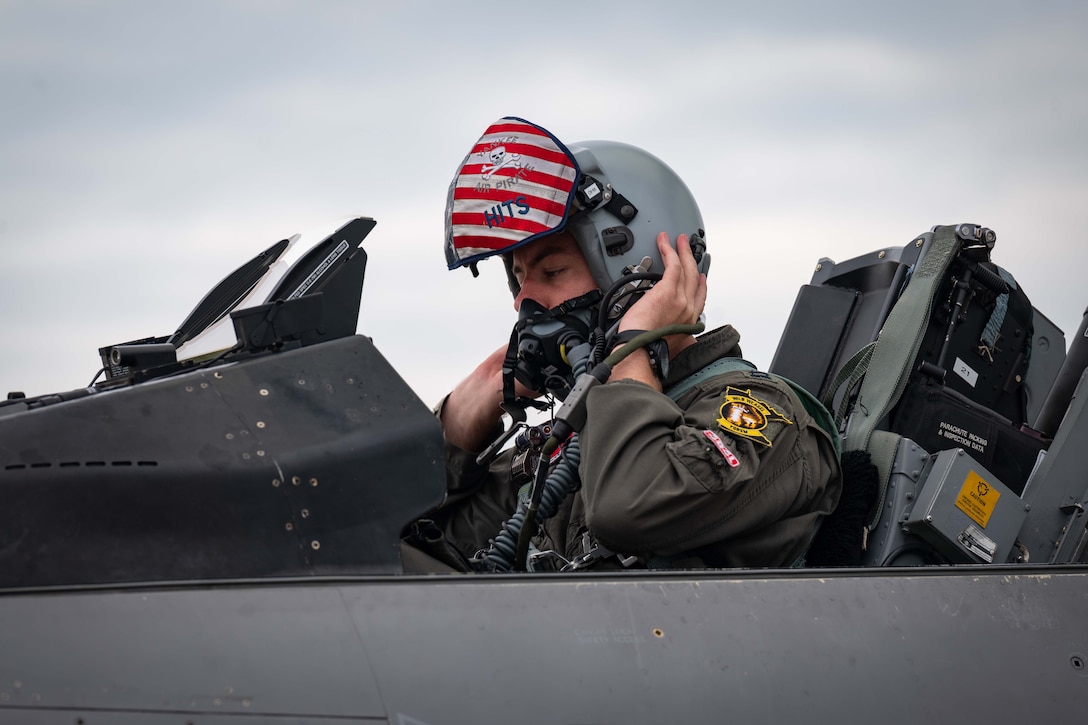 A pilot positions  his helmet while sitting in a plane.