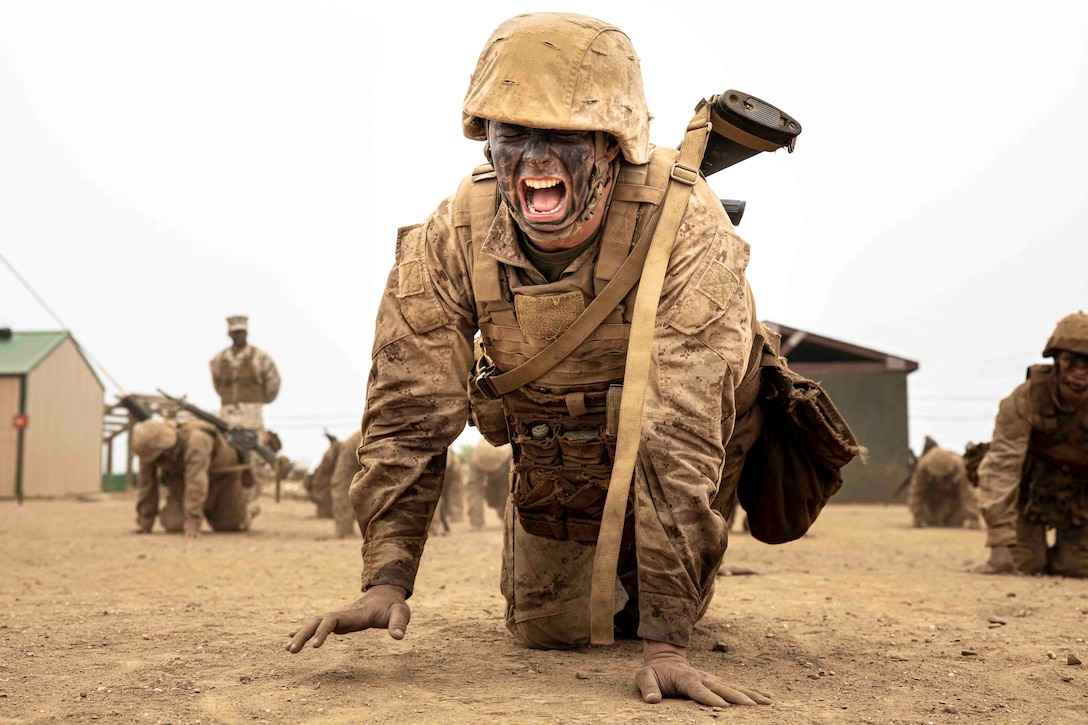 A Marine Corps recruit crawls in front of others while grimacing.