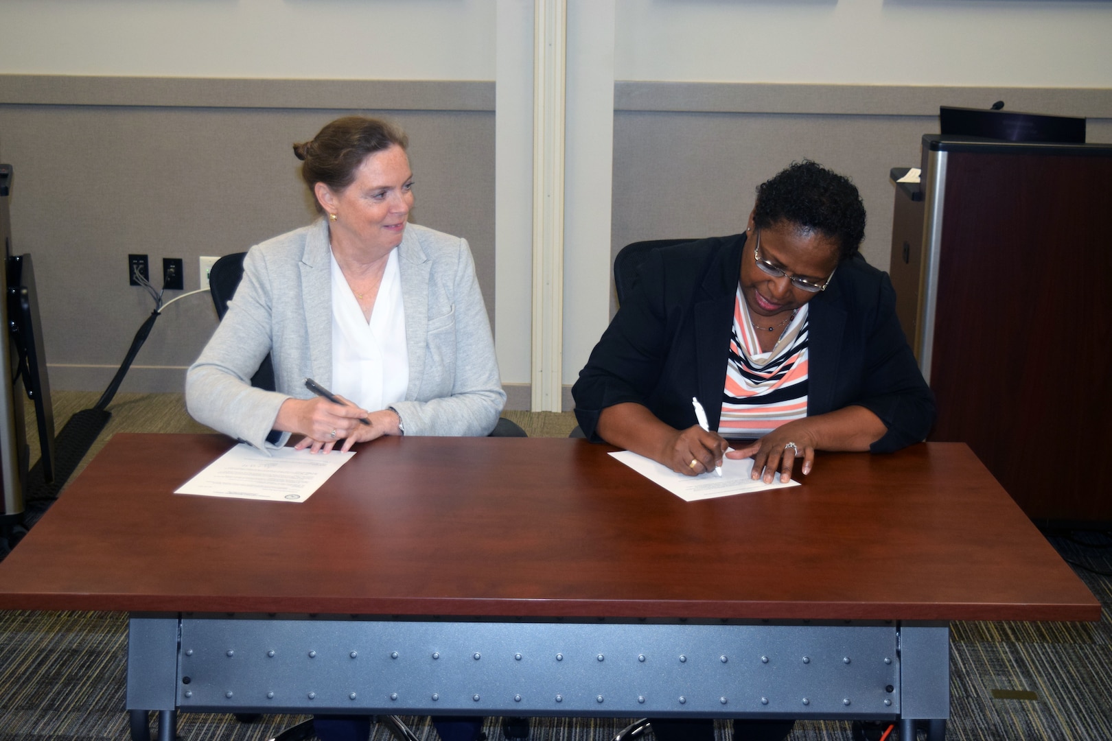 Two women sitting at a desk signing documents