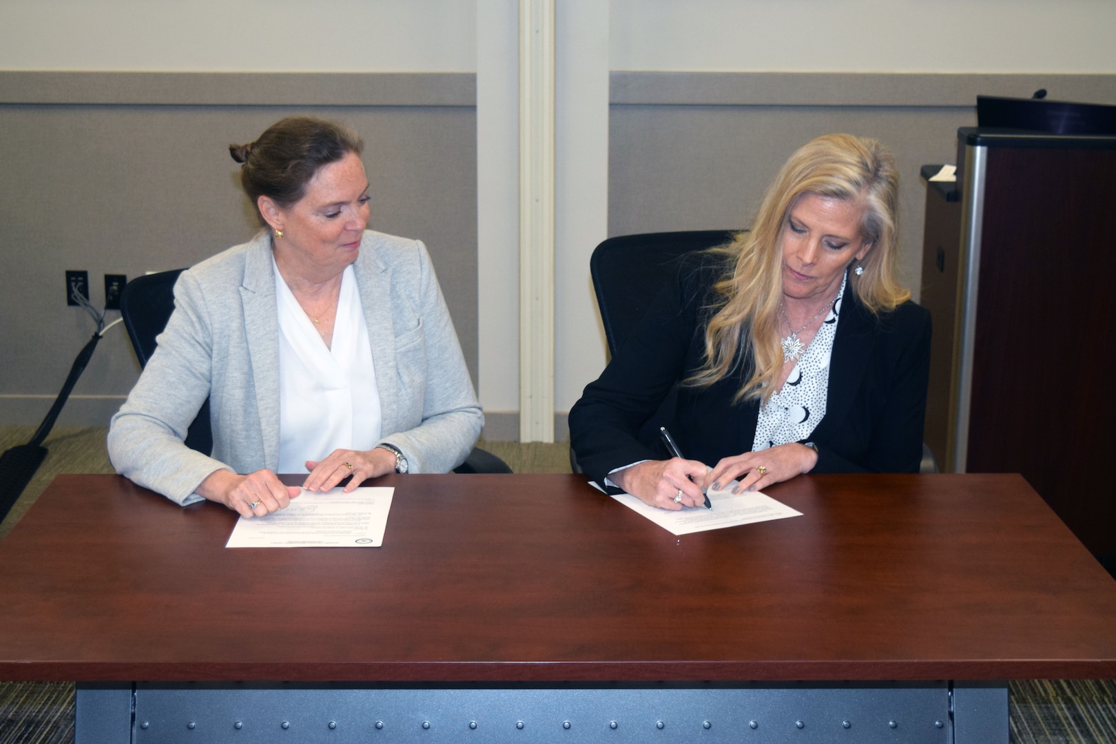 Two women sitting at a desk signing documents.