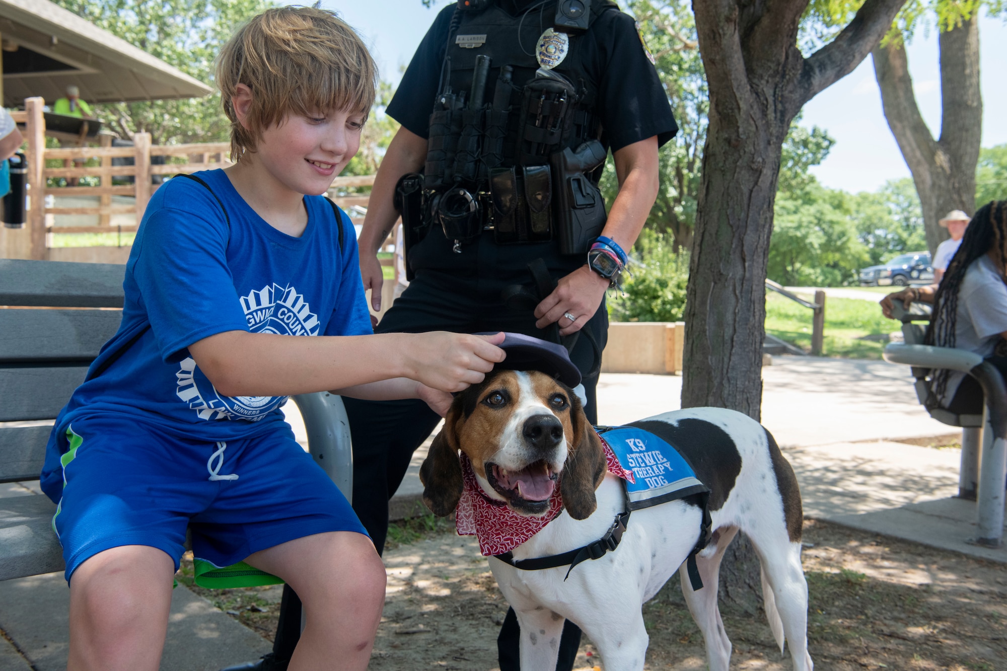 A Camper at L.A.W Camp places his hat on a service dog at O.J Watson Park, Wichita, Kansas July 11, 2023. L.A.W Camp aims to give children an opportunity to interact with law enforcement in a positive manner as well as meet with strong role models while building their self-confidence, learning team-building and life skills. (U.S. Air Force Photo by Airman 1st Class Gavin Hameed)