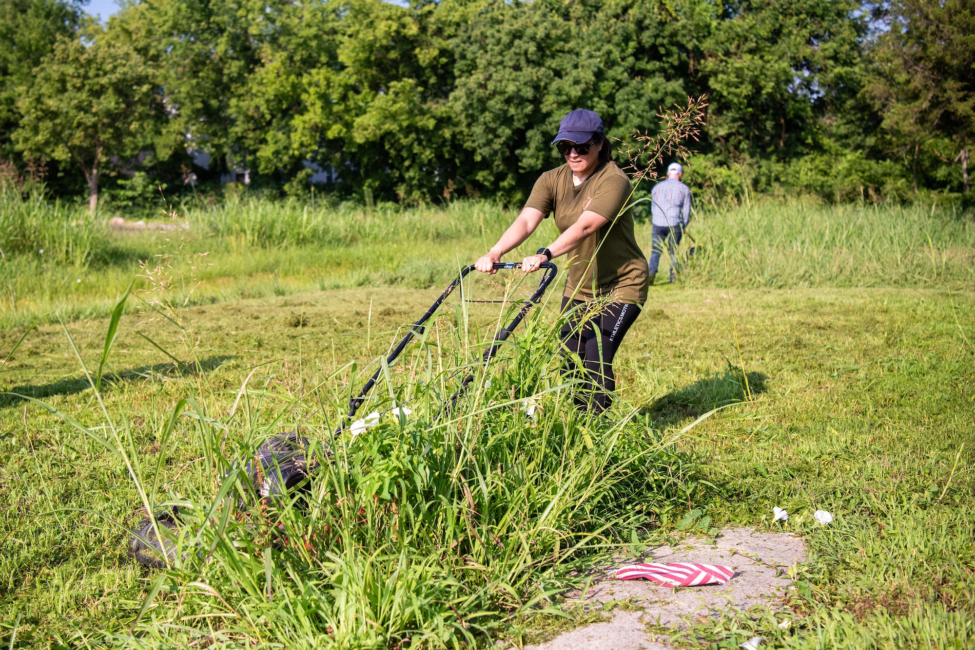 Army Sgt. 1st Class Maria Borja, McDonald Army Health Center, Operations Training non-commissioned officer, mows the lawn at Elmerton Cemetery in Hampton, Virginia, July 8, 2023. The volunteer community relations event helped restore and maintain two of Hampton Roads oldest cemeteries where many African American community leaders and service members are buried. (U.S. Air Force photo by Abraham Essenmacher)
