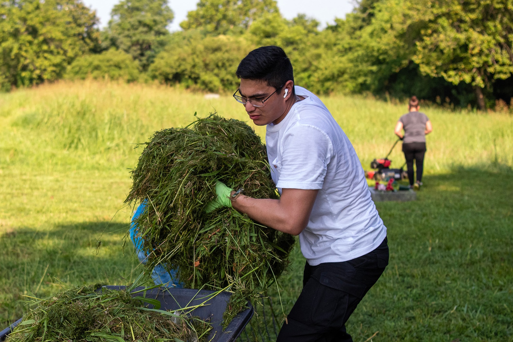 U.S. Army Pvt. Deulin Montanez, 1-210 Aviation Regiment, Advanced Individual Training student, puts grass clippings into a wheel barrel at Elmerton Cemetery in Hampton, Virginia, July 8, 2023. The volunteer community relations event helped restore and maintain two of Hampton Roads oldest cemeteries where many African American community leaders and service members are buried. (U.S. Air Force photo by Abraham Essenmacher)